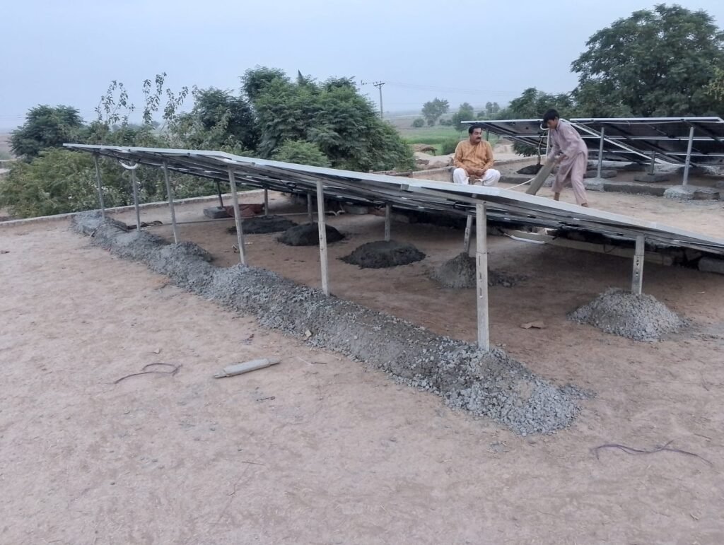Rows of solar panels on raised steel frames with fresh gravel footings, two men working beside them